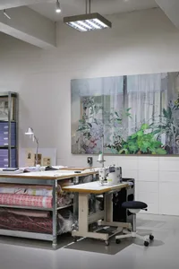 A spacious workstation with a sewing machine, a stool, and shelves of fabric rolls, illuminated by overhead lighting and deco