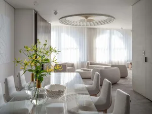 A minimalist living room with white curtains, round coffee table, and fabric cushions.