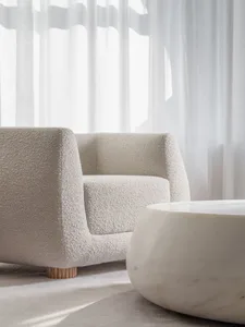 A minimalist living room with a fabric armchair and a marble coffee table.