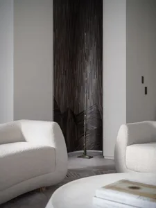 Modern minimalist living room with cream-colored fabric armchairs, marble center table, and abstract sculpture in the backgro