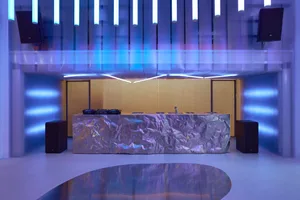 Modern, minimalist DJ booth with metallic surface and futuristic lighting in a club setting.