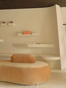 A minimalist bathroom with white concrete walls and a modern orange chair.
