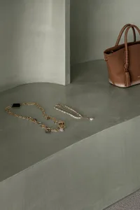 A minimalist fashion accessory setup featuring a brown leather bag, a gold necklace with charms, and a delicate beaded neckla