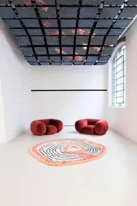 A minimalist interior design featuring two red sofas and a circular rug with concentric circles.