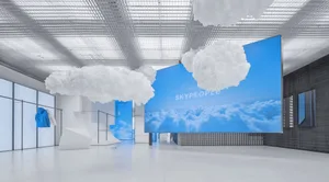 Modern retail space featuring translucent glass and hanging white clouds against a blue sky backdrop.