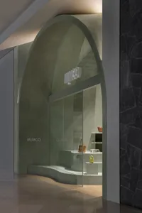 Modern, minimalist storefront with an arched, concrete entrance and a glass window displaying bags.