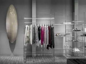 A modern fashion retail store with a translucent clothing rack and glass shelves.