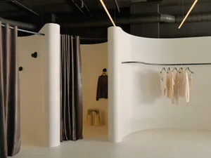 Modern minimalist clothing retail store with beige and brown color scheme and clothing racks.