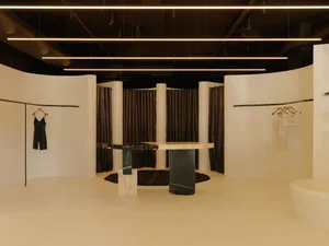 A modern retail shop interior with a minimalist design, featuring a large round marble table and white curved surfaces.