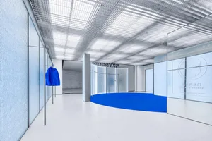 Modern retail storefront featuring a blue carpet, white flooring, and glass walls.