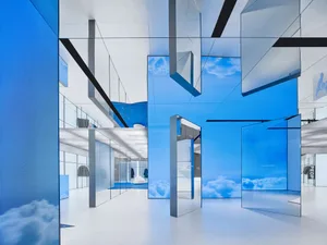 Modern retail storefront featuring large glass mirrors reflecting the sky and clouds.