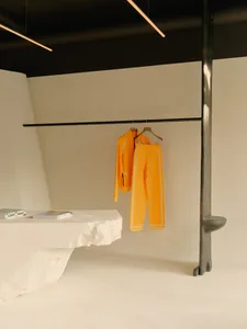 A minimalist interior design featuring an orange tracksuit hanging on a clothes rack in a monochromatic room with a white con