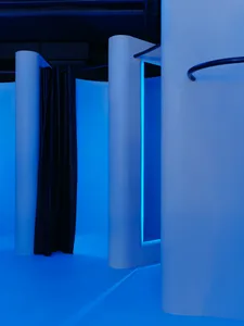 Minimalist architectural space with white panels and blue lighting, photographed with a black curtain.