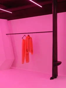 Modern clothing display featuring a bright red jacket and pants hanging on a black rod.