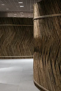 Modern, curved bamboo walls in an indoor space with a concrete floor and overhead lights.