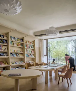 A modern library with wooden shelves and glass walls, featuring comfortable seating and a large window.