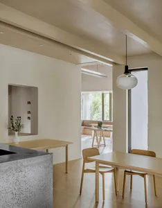 Modern residential living room with wooden furniture and a concrete wall, featuring shadows and natural light.