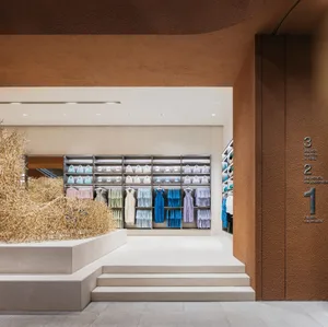 A modern retail storefront with concrete walls and white, pastel, and blue clothing on display.