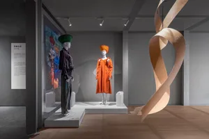 Fashion exhibition display featuring mannequins dressed in modern garments and a large, abstract ribbon-like sculpture hangin