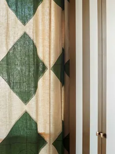 Green and beige patterned curtains hanging from a striped wall.