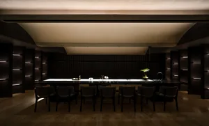 Modern minimalist restaurant interior with a long white dining counter, wood furnishings, and glass details.