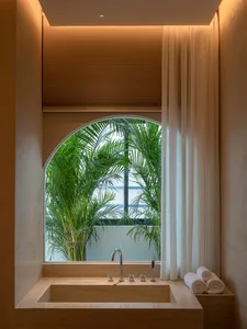 Modern bathroom featuring marble surfaces and tropical plants, with an arched window.