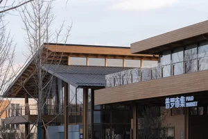 A modern building with a wooden exterior and a metal roof, featuring large glass windows.