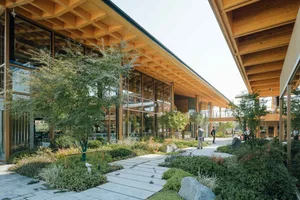 A modern cultural center featuring a wooden facade, large glass windows, and stone elements, surrounded by greenery and pathw