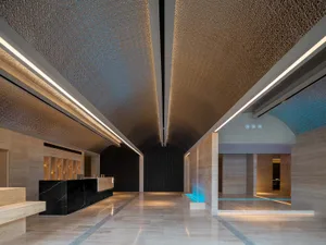 A modern hotel lobby featuring marble floors and walls, with a reception desk and a water feature.