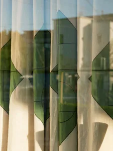 Modern patterned curtains hanging in a window, allowing light to filter through, with a view of the street outside.
