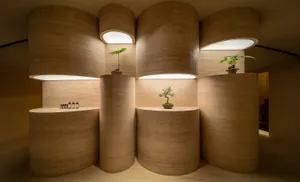 An elegant retail storefront with concrete and wooden columns, featuring bonsai plants on shelves.