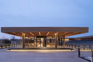 Modern restaurant exterior with wooden beams and glass walls against a clear sky.