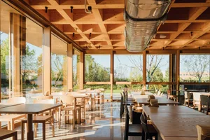 A contemporary industrial cafe interior with wooden tables, chairs, and a glass ceiling