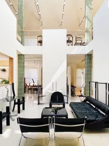 Modern living room with black chairs, coffee table, and sofa on a white floor, glass railings, and green columns.