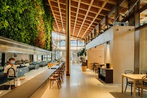 A modern restaurant interior featuring wooden tables and chairs, a living green wall, and large windows.