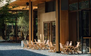 An outdoor setting with wooden tables and chairs, surrounded by natural elements and spacious, open-air architecture.