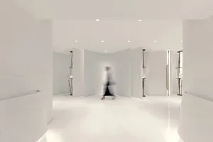A minimalist white interior space with curved walls and a person walking through the corridor.