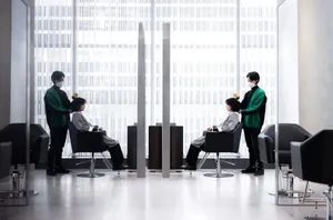 Modern salon setting with clients seated in black chairs, stylists cutting hair.