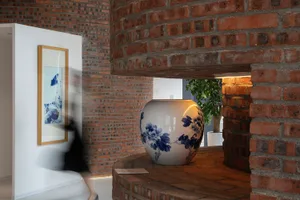 A modern industrial space featuring a large brick column with a large decorative vase and a framed painting on a white wall.