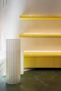 A minimalist retail storefront featuring yellow columns, white shelves, and a white floor.