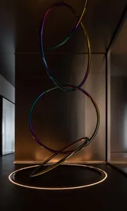 A modern art installation featuring metal rings in dark, reflective material on a dark floor, with ambient lighting highlight