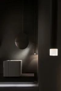 Modern minimalist bathroom with white ceramic sink, round mirror, and wall-mounted light fixture.