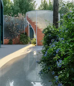 A modern brick structure with a garden in the foreground, featuring blue flowers and a reflective pool.