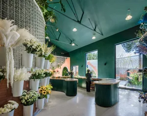 A modern coffee shop interior with green painted walls, brick accents, decorative flowers, and white feather arrangements.
