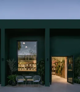 A modern flower shop exterior with green painted walls and large windows displaying various plants.