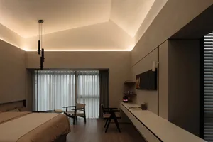 A modern minimalist bedroom with neutral-toned materials, featuring a bed, a desk, chairs, and a wall-mounted work area.