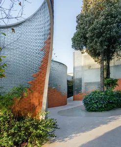 Curved glass and brick facade of a modern urban building with greenery and trees.