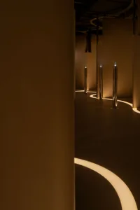 A minimalist installation featuring metallic columns with illuminated lines on a curved floor.