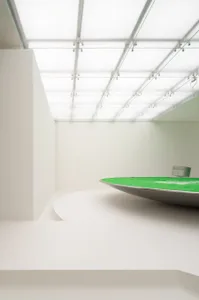 A minimalist white room with a green table and glass ceiling panels.