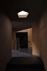 A modern corridor with concrete walls and floor, illuminated by a skylight at the end.